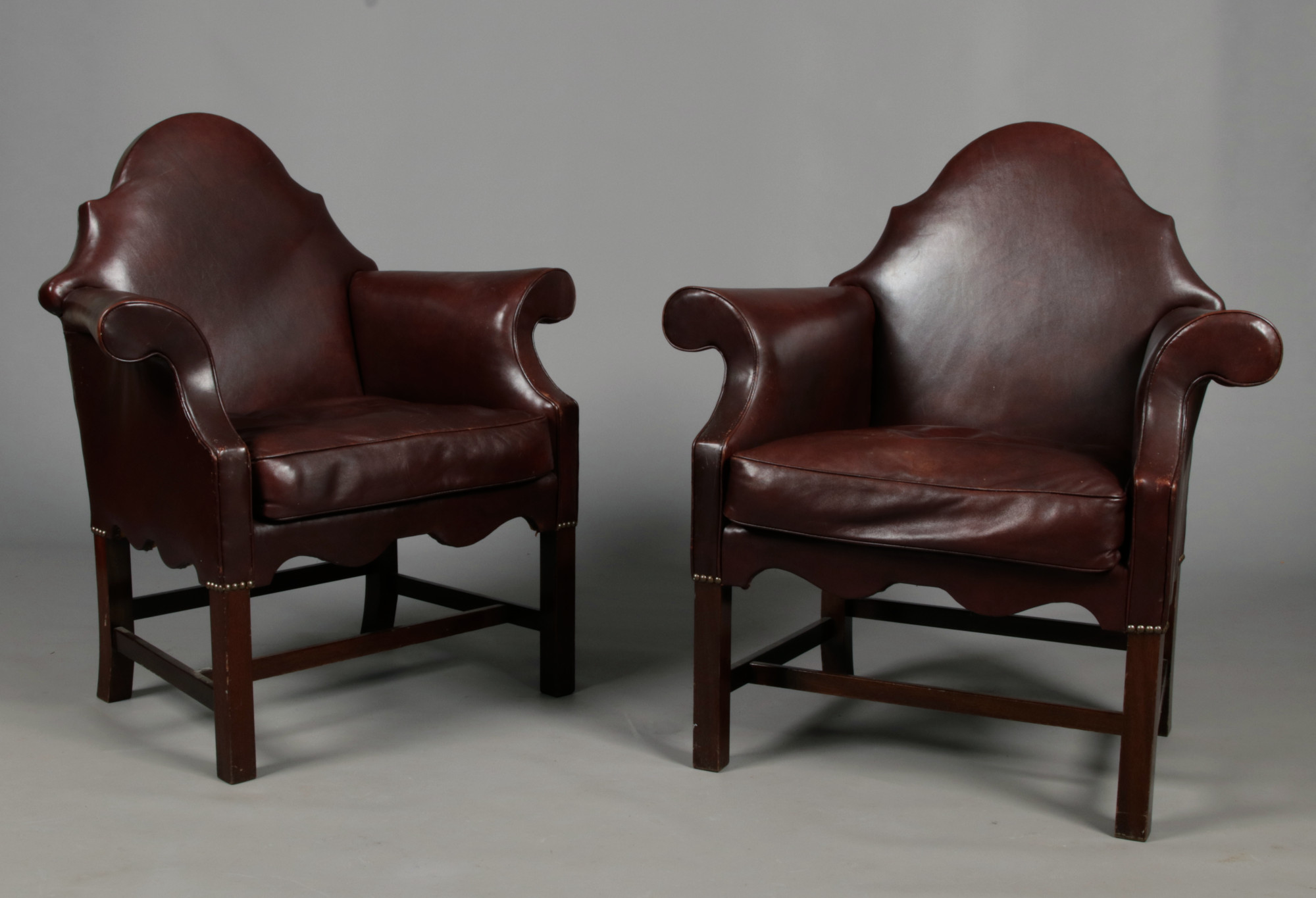 A pair of early 20th century leather upholstered camel back armchairs with brass studwork and raised