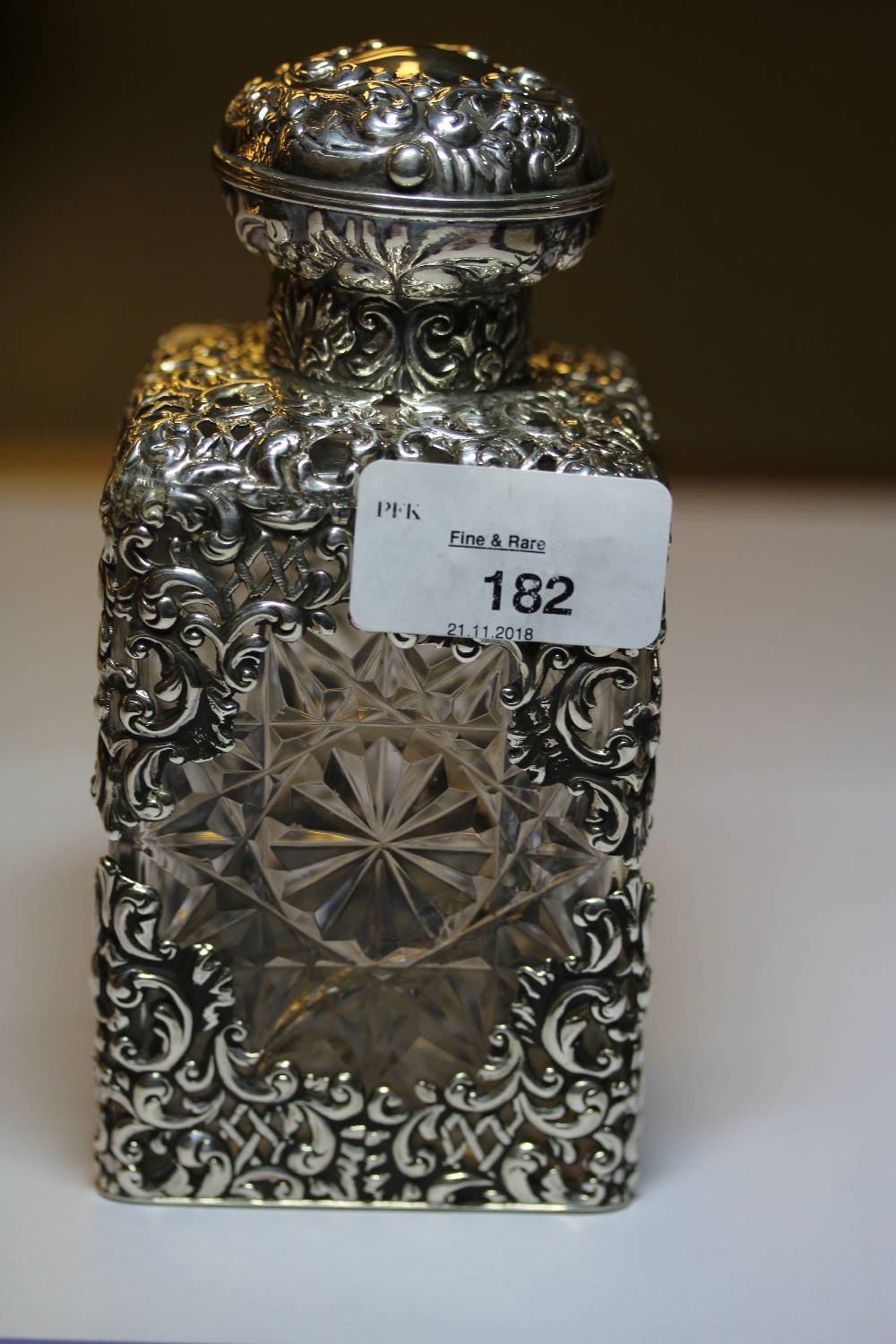 Edward VII embossed silver covered star cut glass scent bottle, the mount by Goldsmiths &