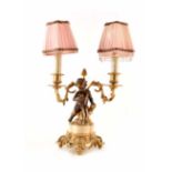 A twin branched table lamp in an ormolu style with gilded detail surrounding a central cherub