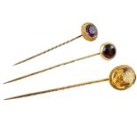 Three yellow gold stone set stick pins, including one set with an oval faceted citrine with rope