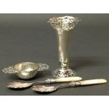 A small silver candlestick holder with pierced decoration, silver tea strainer and two silver spoons