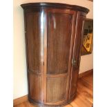 An early 20th century half round wardrobe, the panelled doors opening to reveal hanging space,