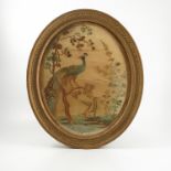 A 19th century oval tapestry picture, on silk, of a peacock in a tree with another bird flying,