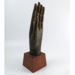 An Eastern metal model, of a hand, with remains of gilt decoration, on a wooden base,