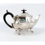 A silver tea pot, of shaped oval form, with wooden scroll handle, raised on four scroll feet,