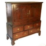 A mid 18th century oak press cupboard, with arched panel cupboards, over five drawers, raised on