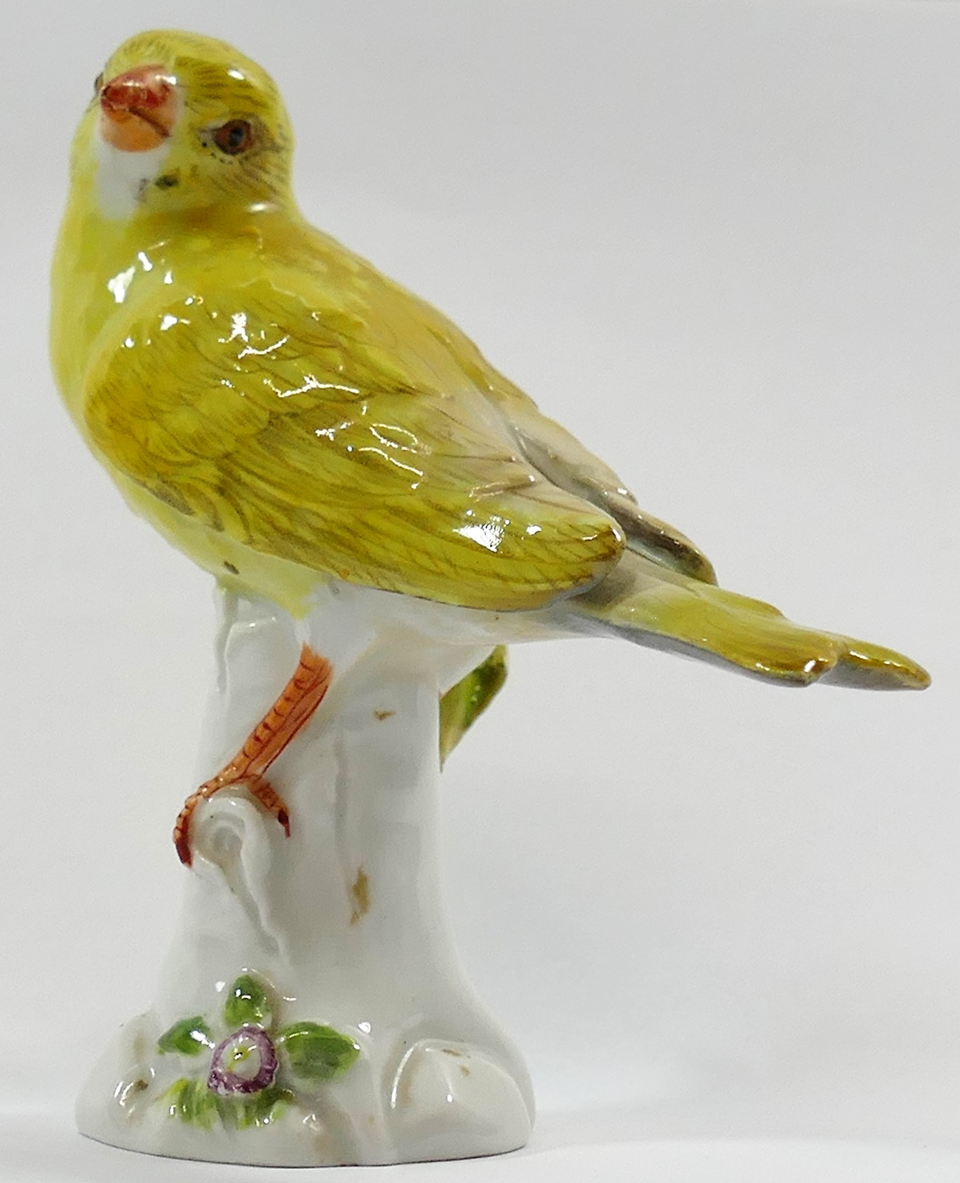 A porcelain figure of a yellow canary, perched on a tree stump,