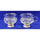 A matching glass cream jug and sugar bowl with hand engraved decoration and silver coloured metal