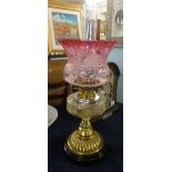 An oil lamp, with clear glass reservoir, brass base and black plinth with cranberry etch glass shade