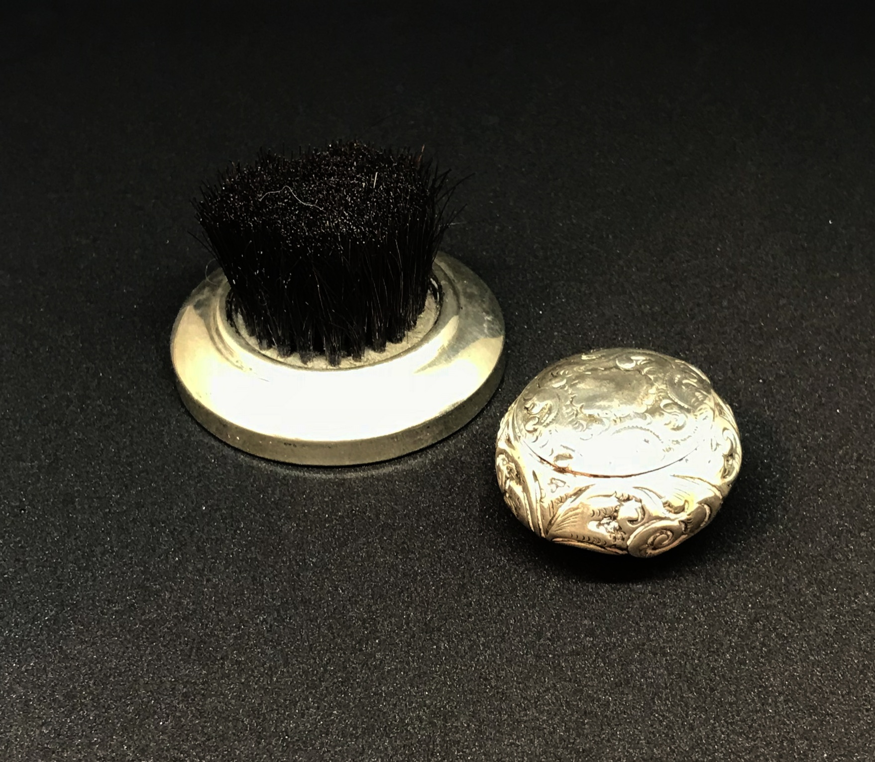 A silver and embossed round pill box and a silver finger brush (2).