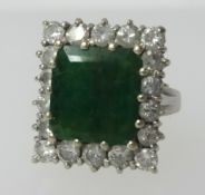 An 18ct white gold ring set with a large square cur emerald within a diamond border, finger size L/