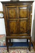 An antique English joined oak cupboard on stand with single moulded panel door, enclosing two shaped