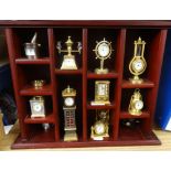 A collection of miniature brass clocks in display cabinet.
