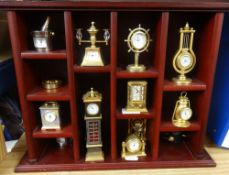 A collection of miniature brass clocks in display cabinet.