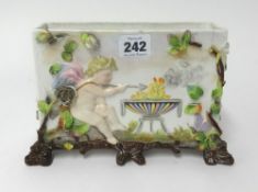 A porcelain rectangular box decorated in relief with a winged cherub over a cauldron with flowers