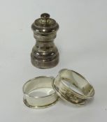 A pair of silver napkin rings and a silver pepper grinder.