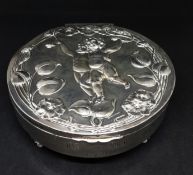 An Edwardian round silver trinket box the hinged lid depicting two cherubs within a flower and