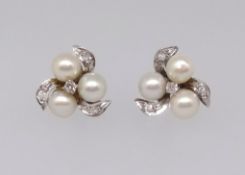 A pair of white gold pearl and diamond earrings, each comprising a trefoil of cultured pearls