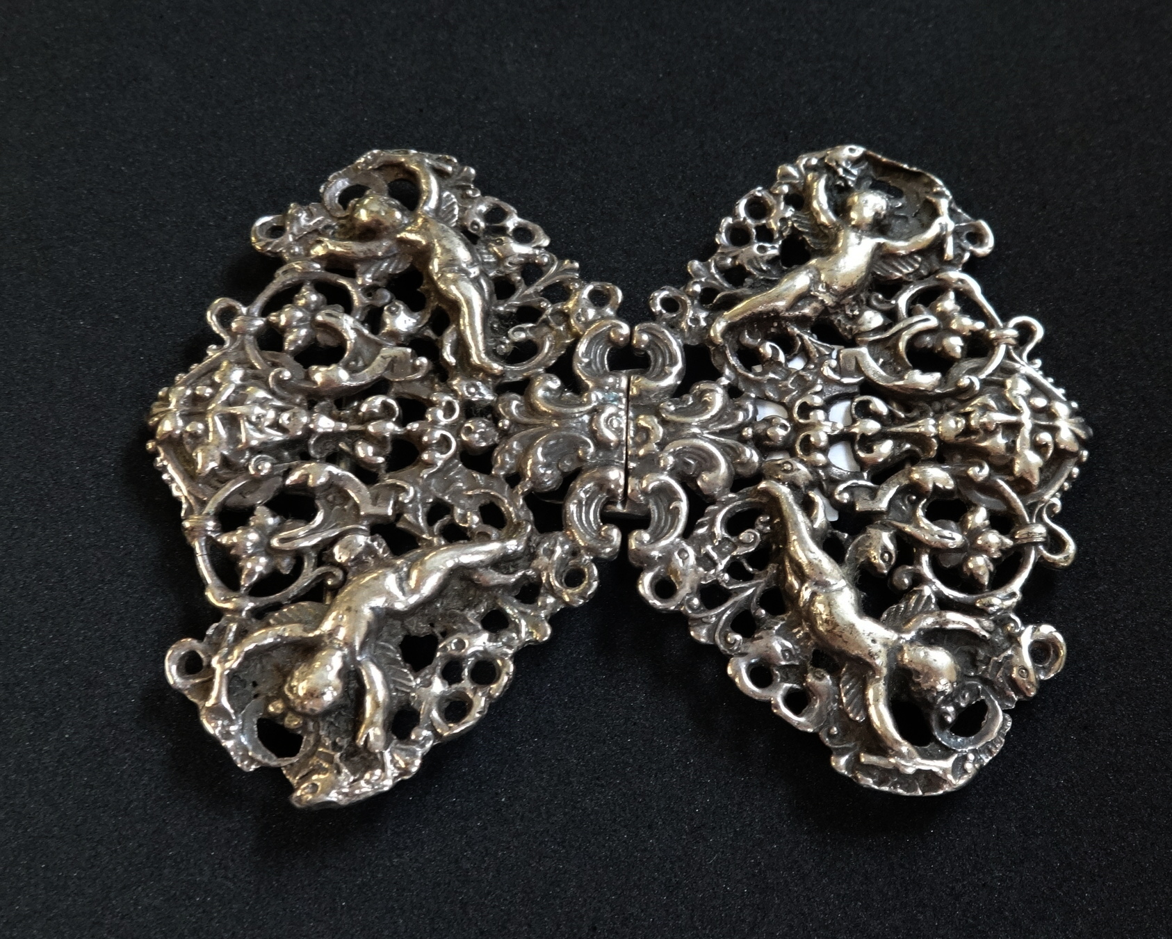 An ornate silver nurses buckle decorated with cherubs.