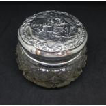 A silver top jar the lid with embossed decoration of figures within a scroll work border.