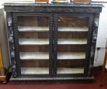 A late Victorian heavily carved dark oak free standing and glazed bookcase, width 120cm