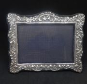 A silver photo frame with embossed decoration with scallop shells and scroll work 18cm x 15cm