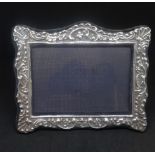 A silver photo frame with embossed decoration with scallop shells and scroll work 18cm x 15cm