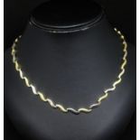 An 18ct necklet set with alternate yellow and white gold fancy wave design, links stamped 750, 28.