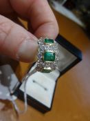 A fine emerald and diamond ring set with three emeralds within an arrangement of twenty four