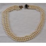 Triple strand necklace of cultured pearls with a 9 carat gold oval clasp set with a red glass