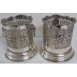 A pair of silver plated bottle holders or coasters, cylindrical bodies with scrolled piercing, on
