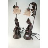A pair of bronzed figural table lamps with glass shades