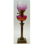Early 20th century Corinthian column brass oil lamp with cranberry glass reservoir and shade.