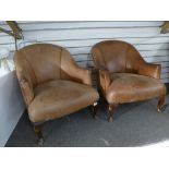 A pair of brown leather tub chairs on cabriolet legs.