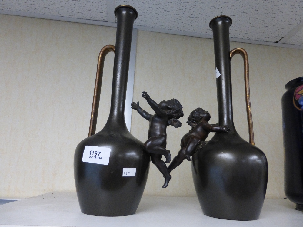 A pair of long handled vases decorated with cherubs