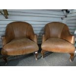 A pair of brown leather tub chairs on cabriolet legs.