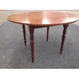 A circular pine dining table raised on turned tapering legs.