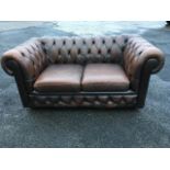 A brown leather button upholstered chesterfield sofa, with loose cushions, raised on casters.