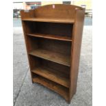 An arts & crafts oak open bookcase with arched back above adjustable shelves, having conforming