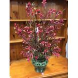 A decorative artificial flower arrangement, the red plant in embossed verdigris brass vase.