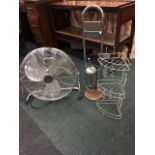 A large chrome electric fan on adjustable stand; a corner bathroom soap stand with three trays;