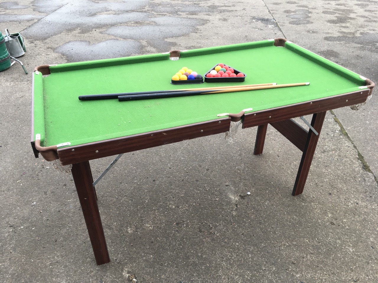 A folding pool table, the baize lined top with brass pockets, complete with cues, balls, triangle,