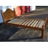 A pine single bed with arched panelled headboard framed by square cornerposts with ball finials, the