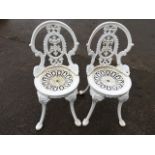 A pair of garden chairs with spade shaped backs framing foliate pierced splats, the circular