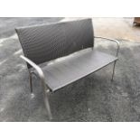 A two-seater 4ft rectangular garden bench of woven style with metal arms.