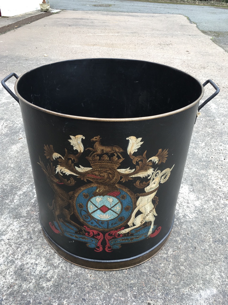 A large tubular log bin, the tub with handles and rolled rim decorated with armorial stye crest. (