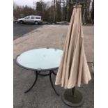 A circular glass topped garden table on sabre legs, complete with central telescopic sunshade on