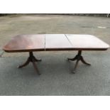 A Georgian style twin pedestal mahogany dining table, the rounded crossbanded top with spare leaf