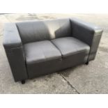 A faux-leather two-seater sofa, with padded back and square platform arms, raised on tubular legs.