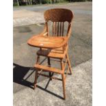 A childs oak high chair with scrolled carving to back rail above spindles, having hinged feeding